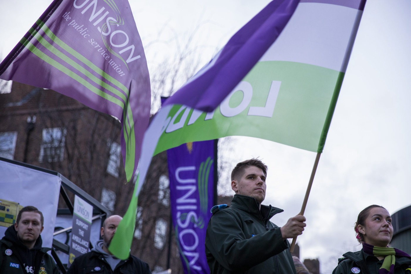 London Ambulance Service UNISON members on the picket line holding the branch's purple-and-green banners aloft during the 2023 ambulance workers' strike.
